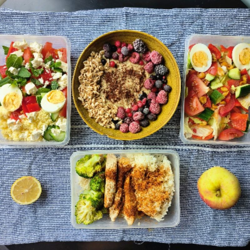 Meal prep op een blauw kleed: havermout met bessen, salades en kip met broccoli